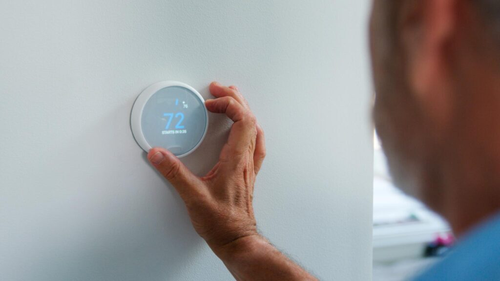 Man Adjusting Digital Central Heating Thermostat In Home